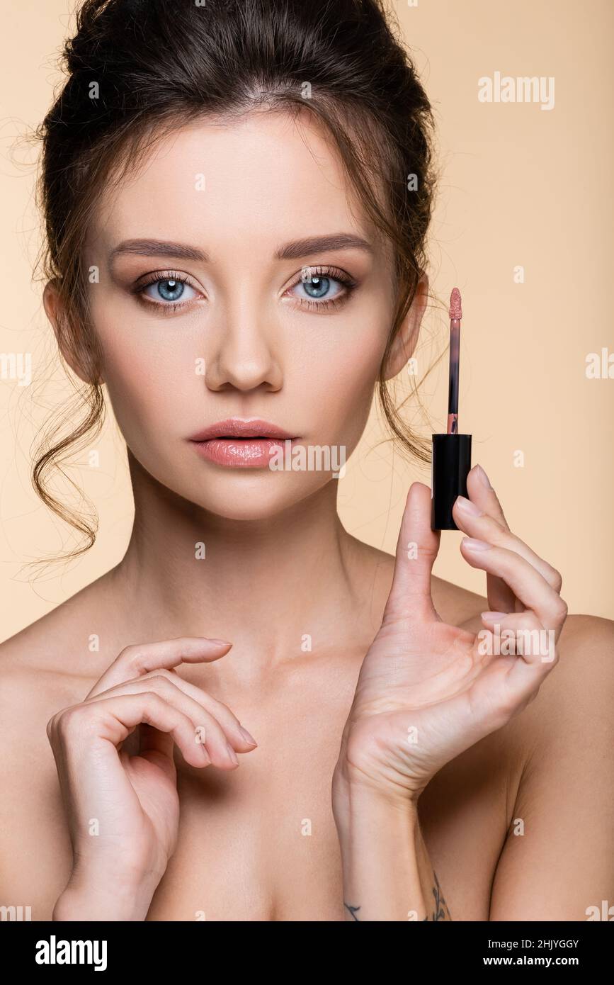 Portrait of pretty model holding brush of lip gloss and looking at camera isolated on beige Stock Photo