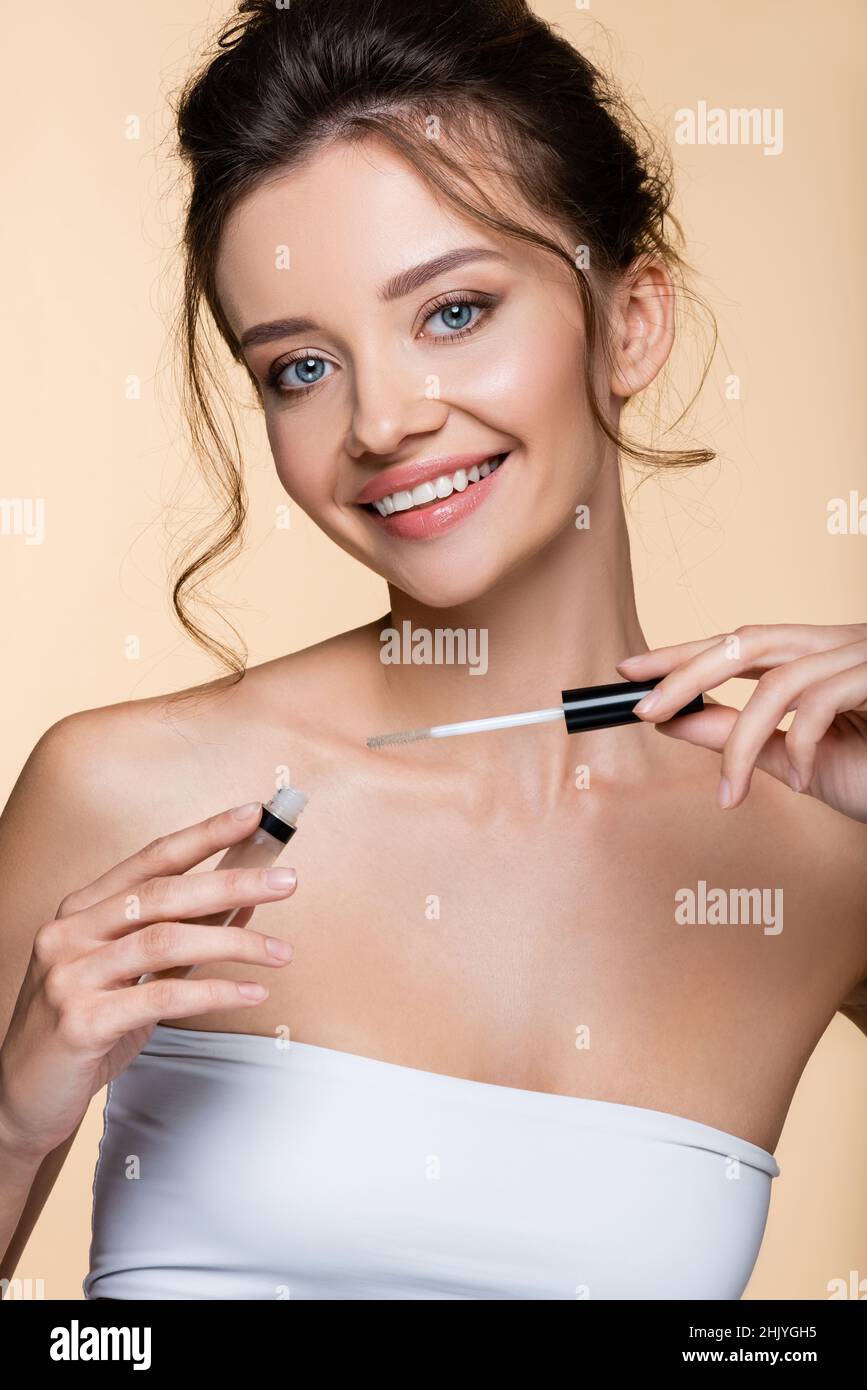 Pretty model in white top holding eyebrow gel isolated on beige Stock Photo