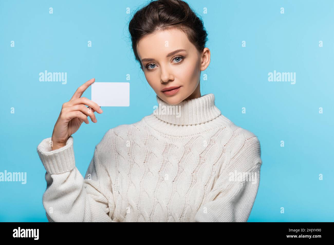 Model in white sweater holding blank card isolated on blue Stock Photo