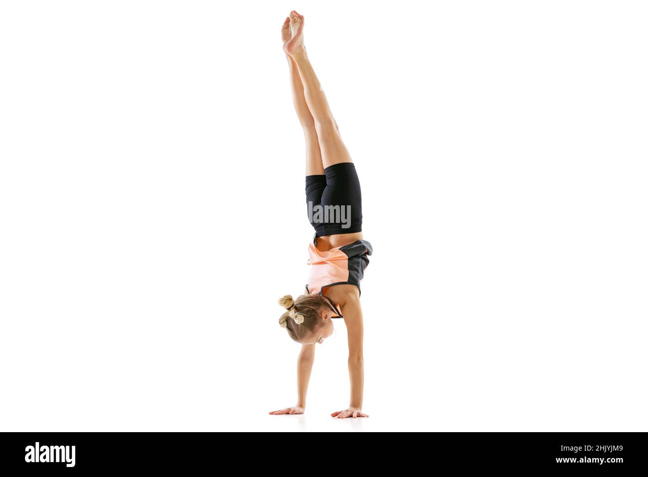 Portrait of sportive young girl, rhythmic gymnastics artist doing a handstand isolated on white studio background. Grace in motion, action. Stock Photo