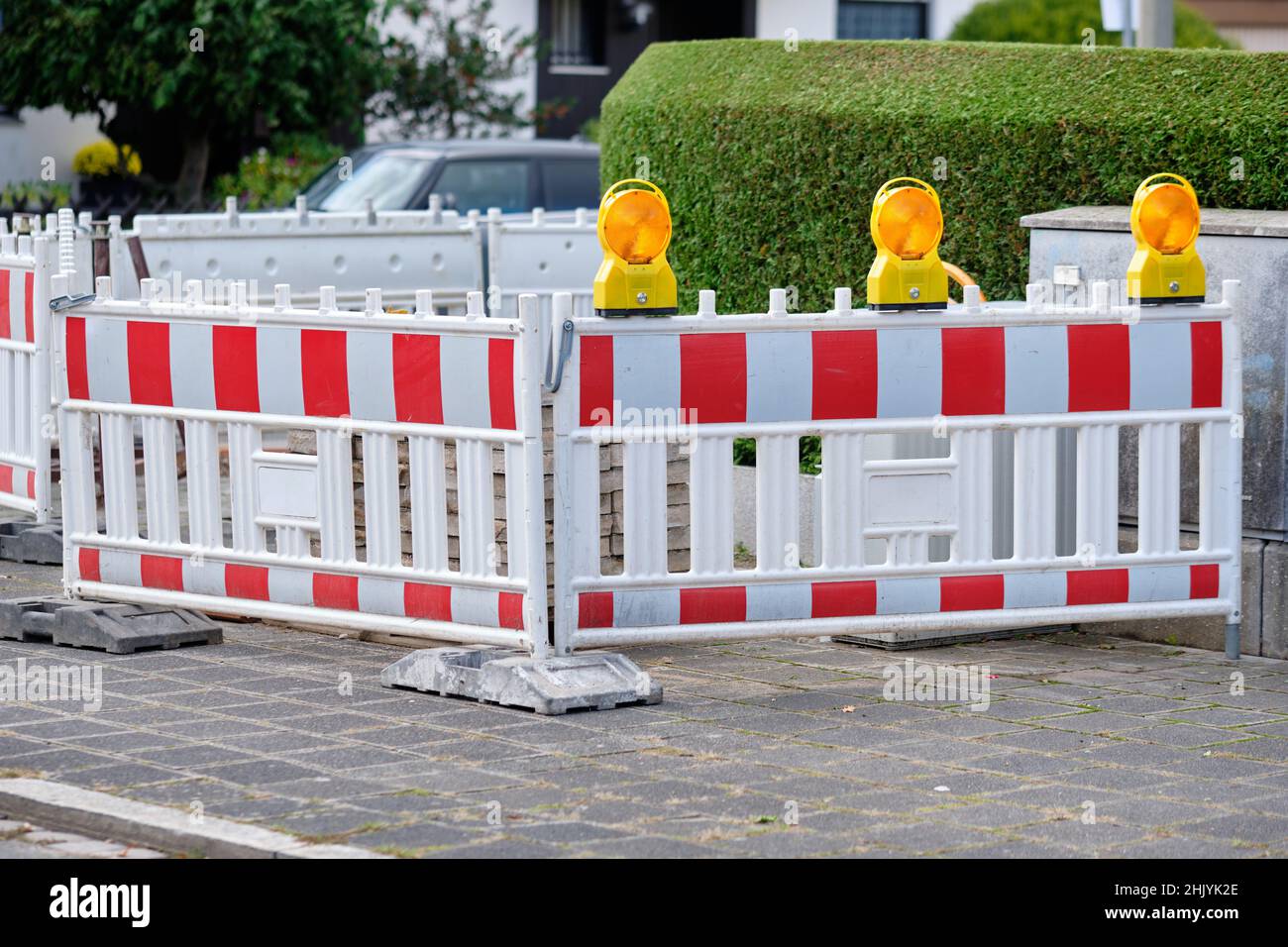 Street barriers with yellow warning lights standing in front of a construction site on the pavement in front of a green hedge. Seen in Germany in Octo Stock Photo
