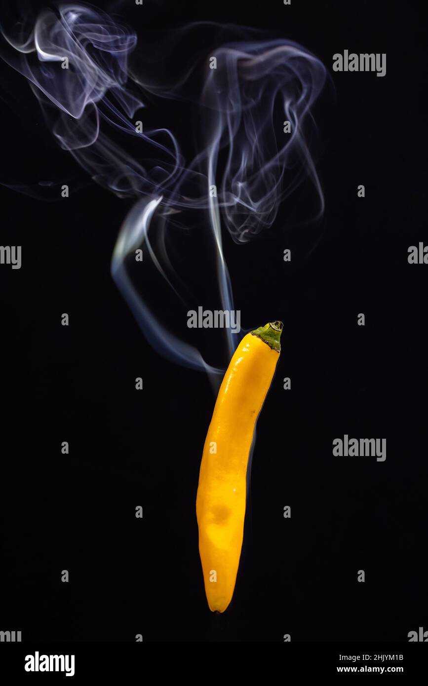 Yellow hot Mexican chili peppers against a black background with smoke