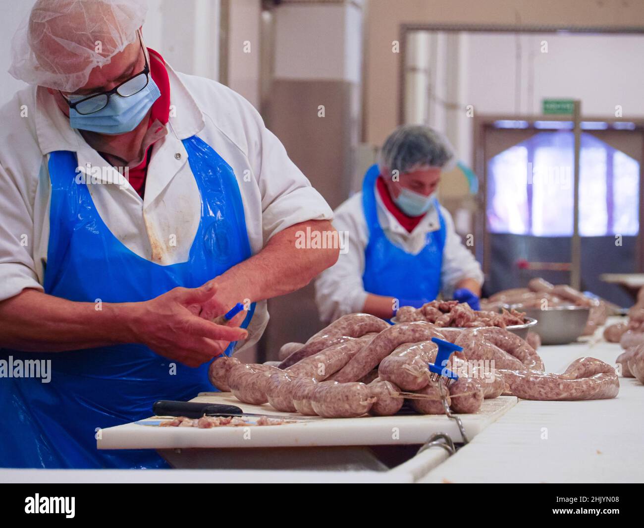 worker manufacturing, stuffing and tying sausages, salme and chorizo in cured meats production facility Stock Photo