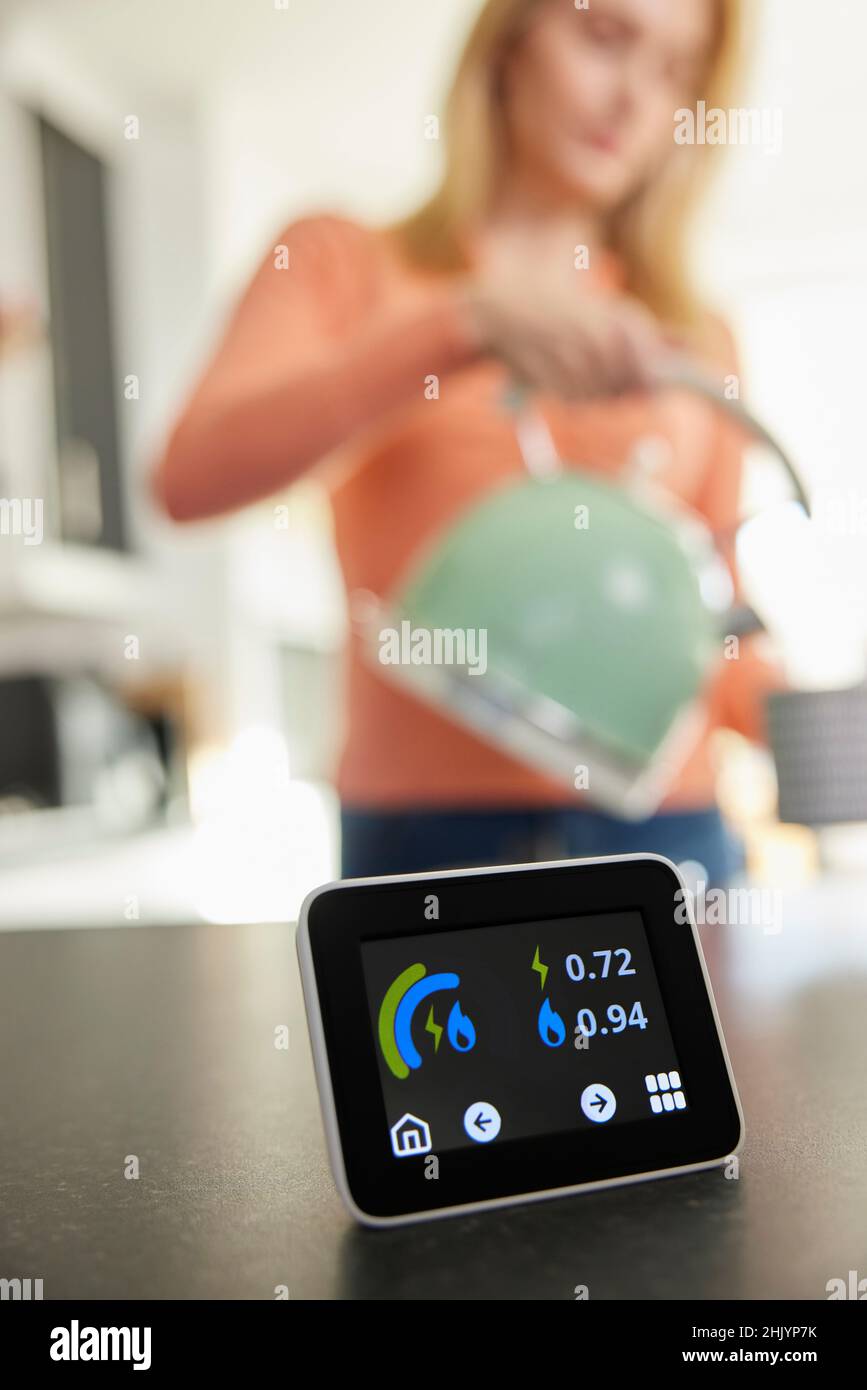 Close Up Of Smart Energy Meter In Kitchen Measuring Electricity And Gas Use With Woman Boiling Kettle Stock Photo