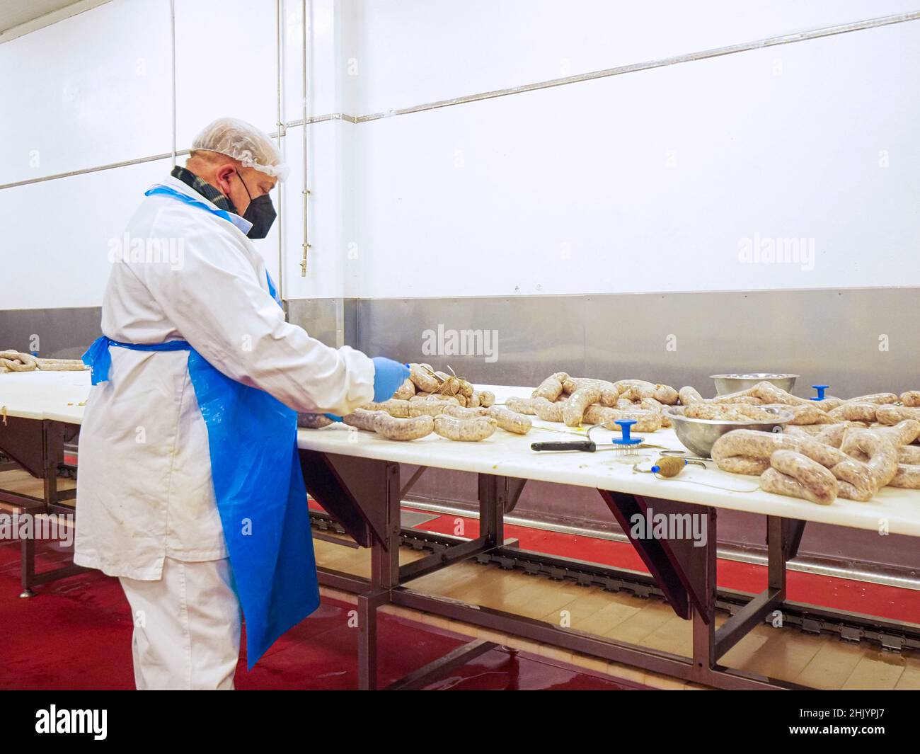 Factory Stuffing worker manufacturing, stuffing and tying sausages, salme and chorizo in ...