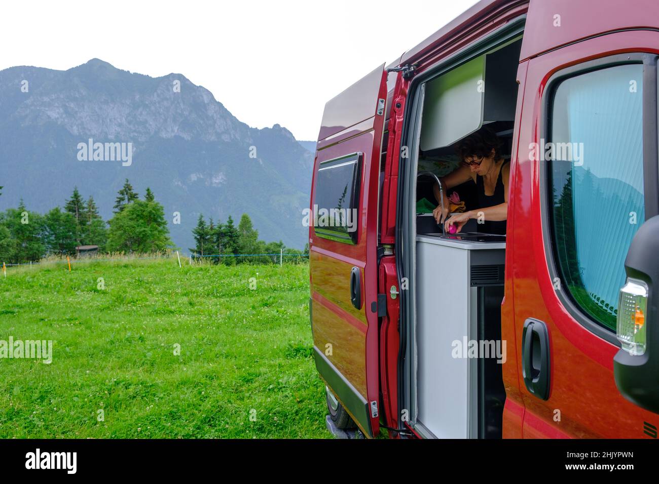 Woman washing dishes on a camper van parked in a field in Val Seriana, Bergamo, Italian Alps Stock Photo
