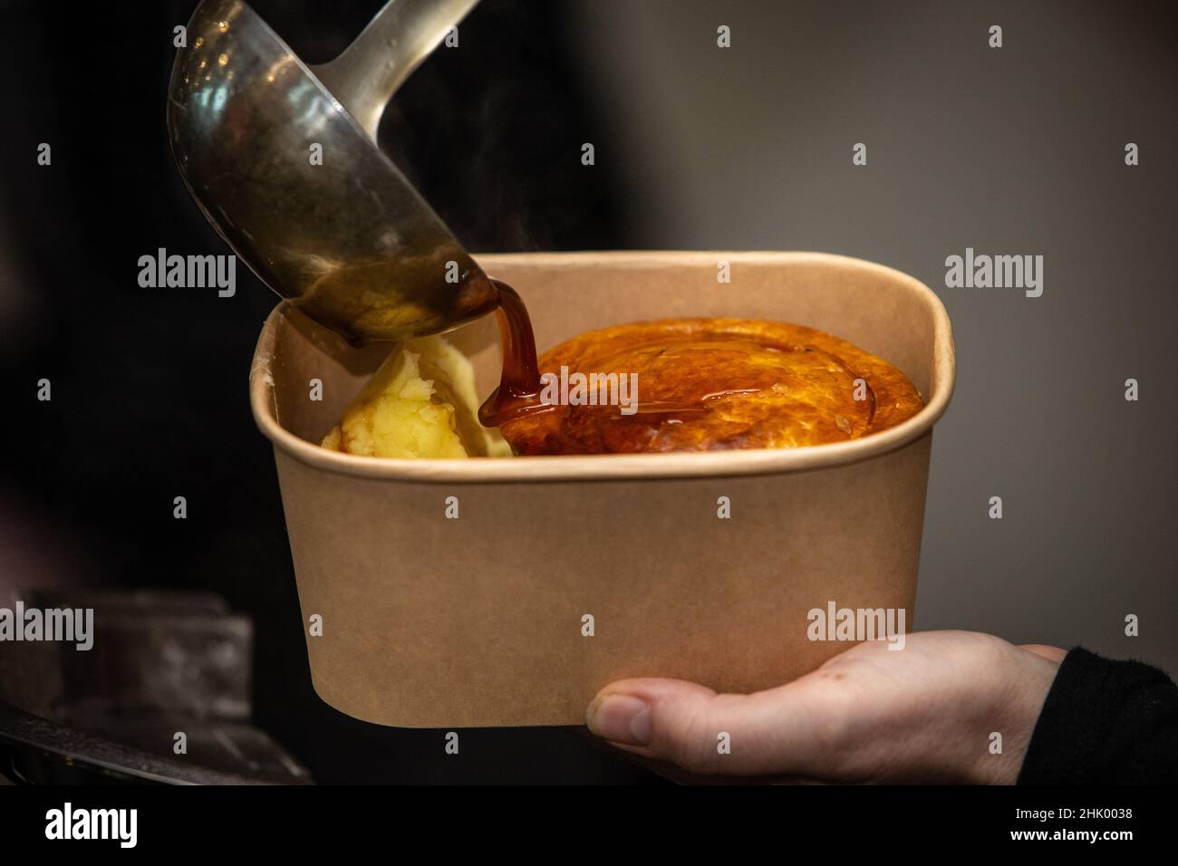 Close up of gravy being poured onto pie and mash potatoes and served in eco friendly tub. Stock Photo