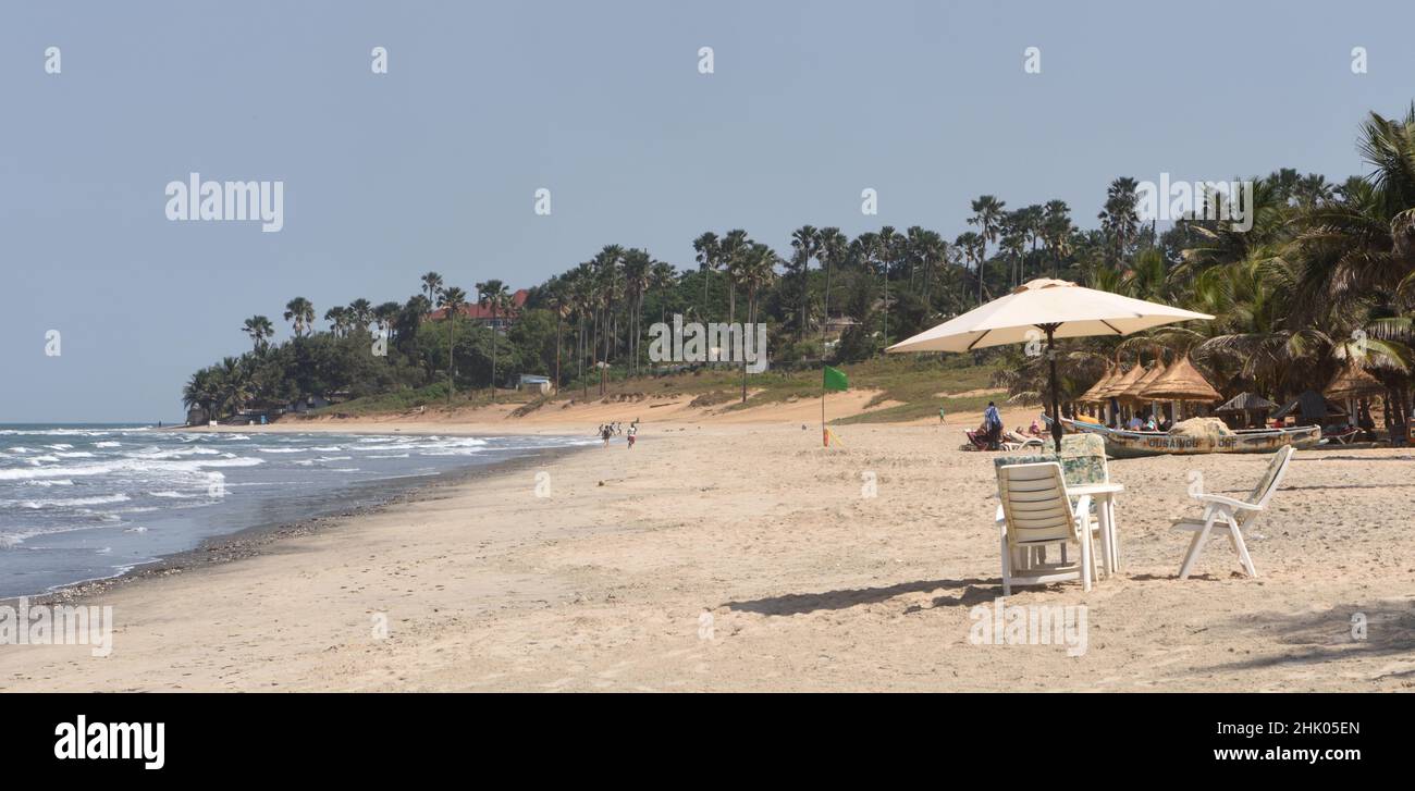 A single unoccupied table and sunshade in front of fishing boats on the palm tree lined sandy beach at Kotu. Kotu, The Republic of the Gambia. Stock Photo