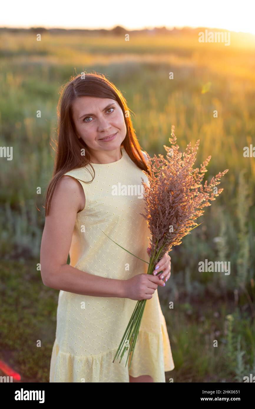 A young woman with a bouquet of field spikelets at sunset Stock Photo