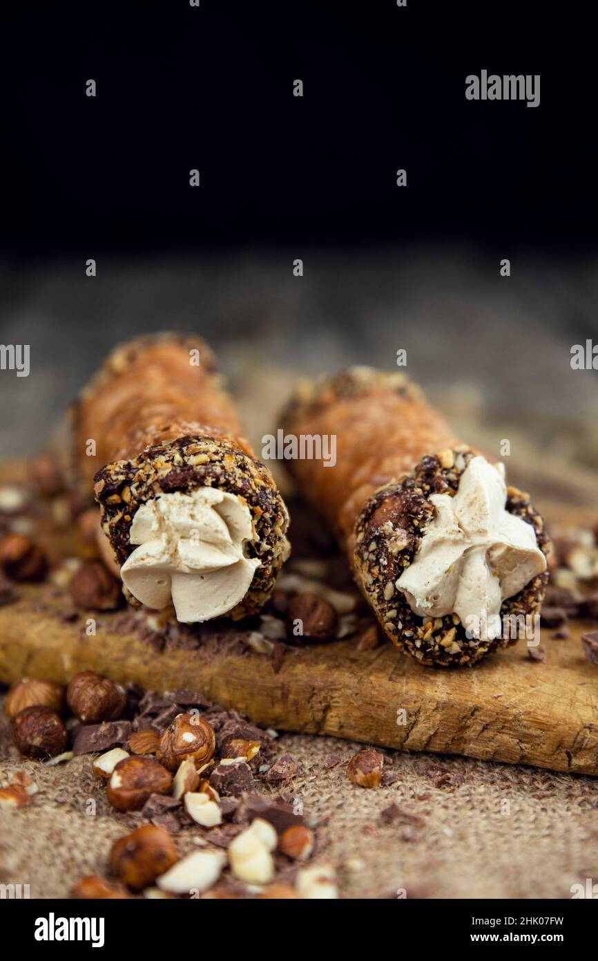 Cannoli, deep fried Italian delicious pastry tubes with a sweet ricotta cheese, chocolate chips and hazelnuts served on a wooden board. Stock Photo