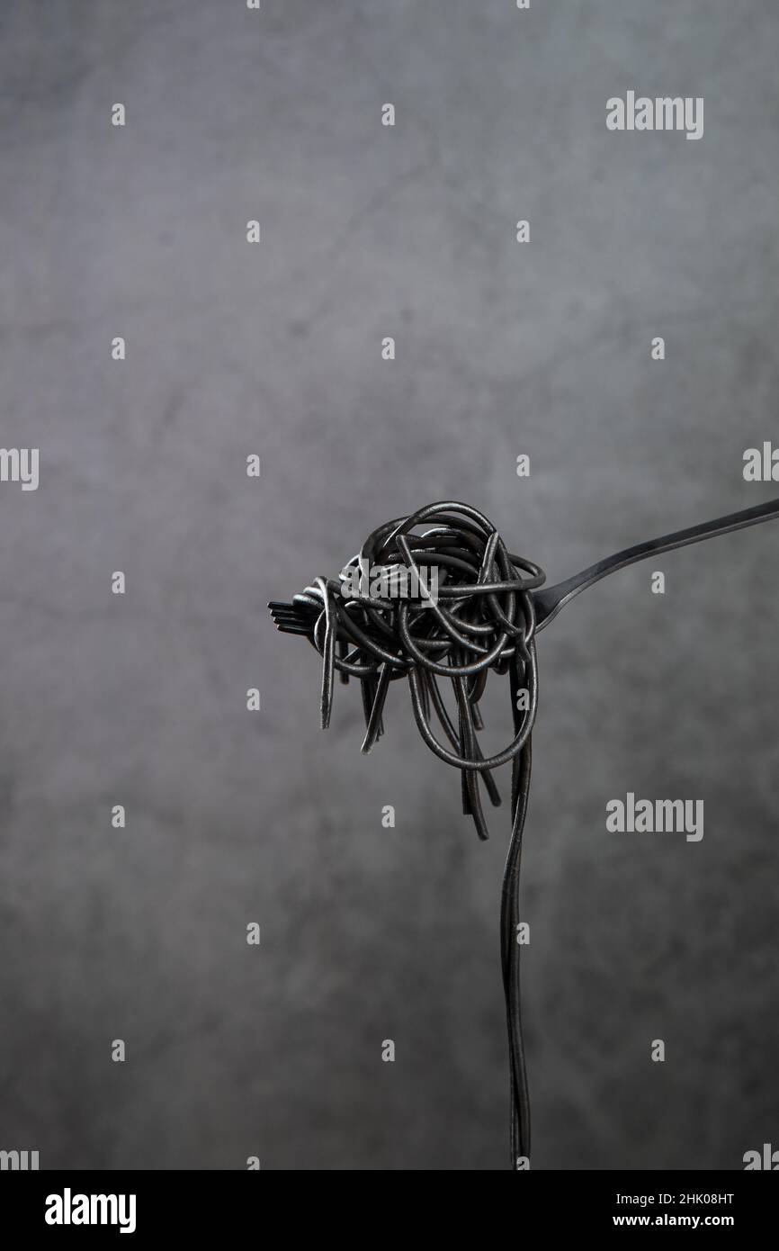 Hot black pasta rolled on a fork on gray background with copyspace. Vertical format. Stock Photo