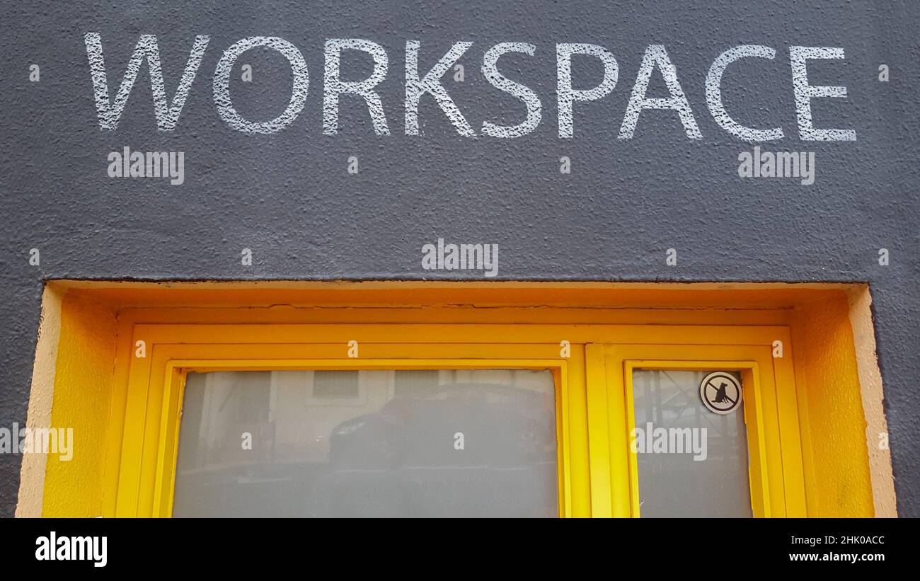 Workspace sign painted over iron yellow door. Banned dogs sticker on right corner. Stock Photo
