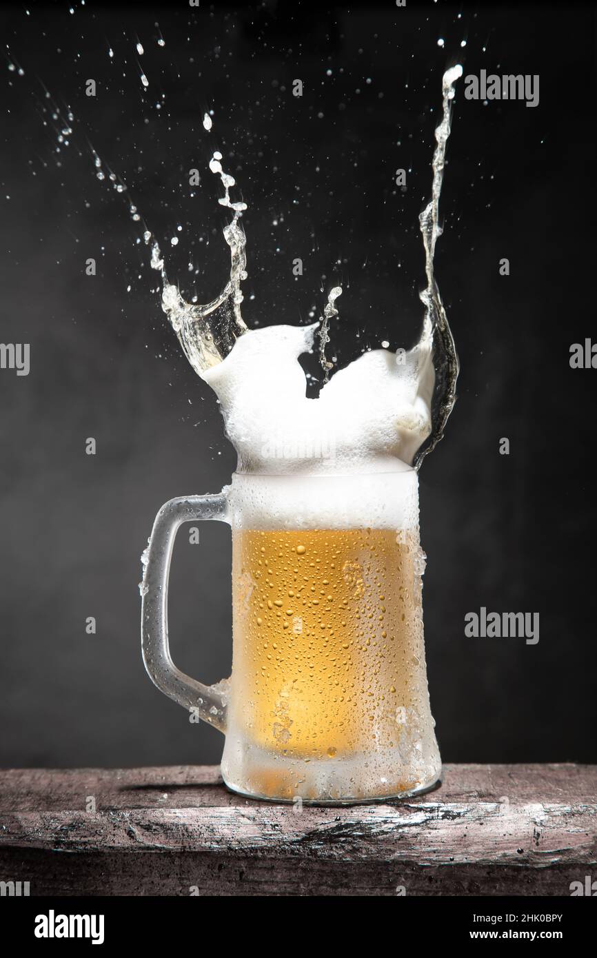 Mug of beer with foam and splashes on wooden table isolated on dark background. Vertical format. Stock Photo