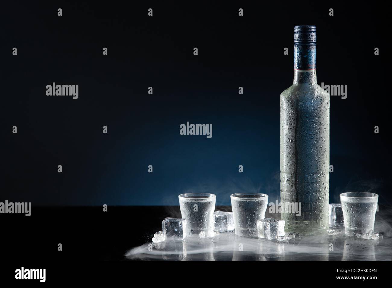 Ice-cold bottle of vodka with shot glasses on dark blue background with copy space. Stock Photo