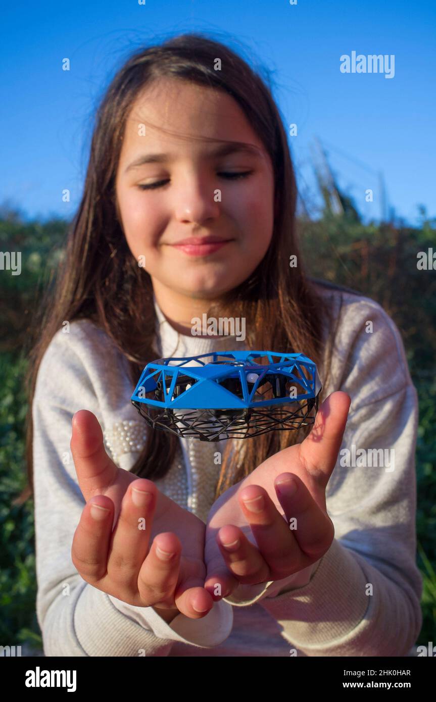 Little girl playing with toy dron. Little quadcopter flying over her hands. Stock Photo