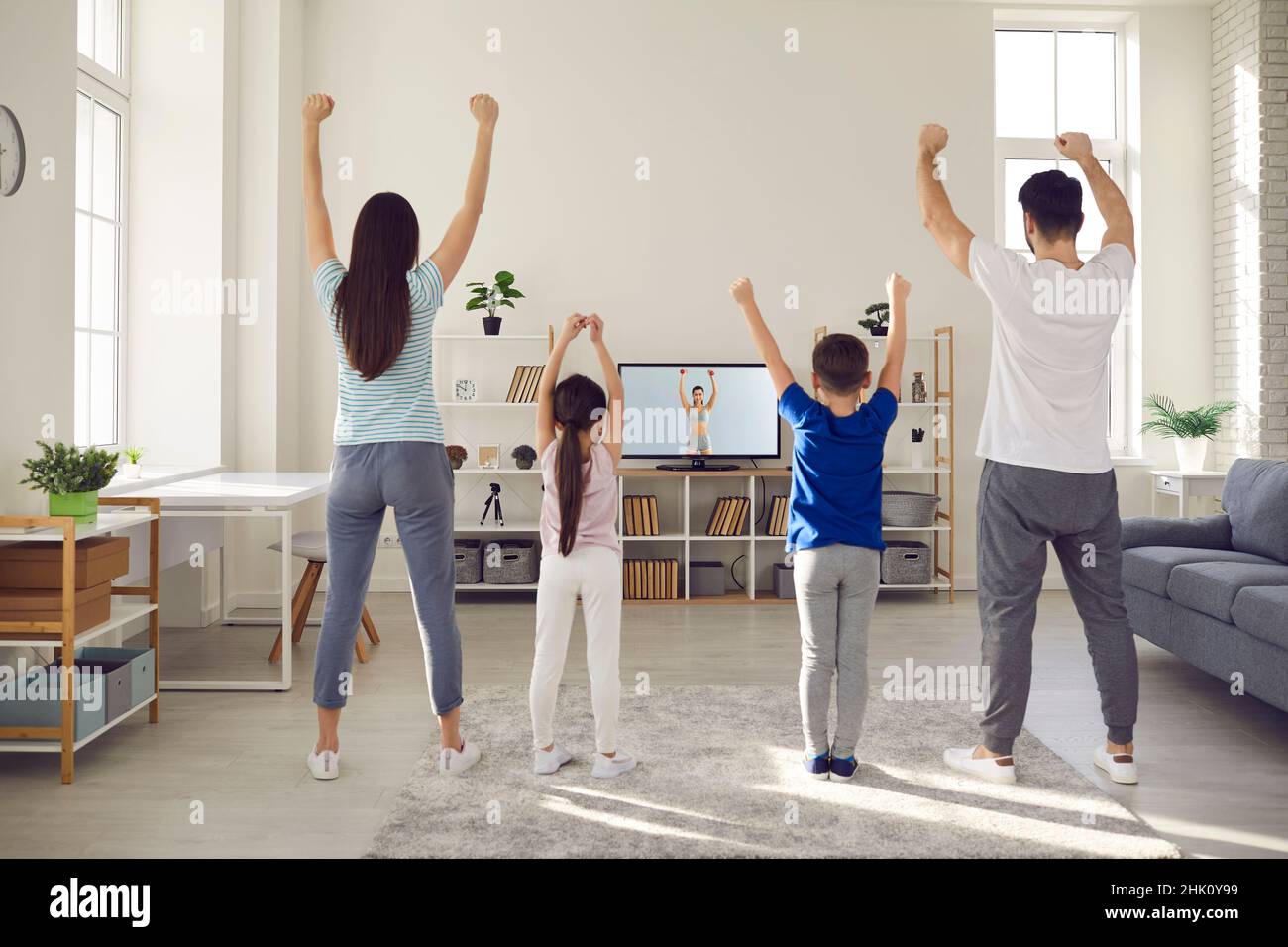 Family watching a workout video lesson on TV and doing fitness exercises together Stock Photo