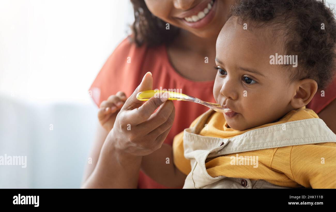 Baby Nutrition Habits. Smiling Black Mother Feeding Cute Infant Boy