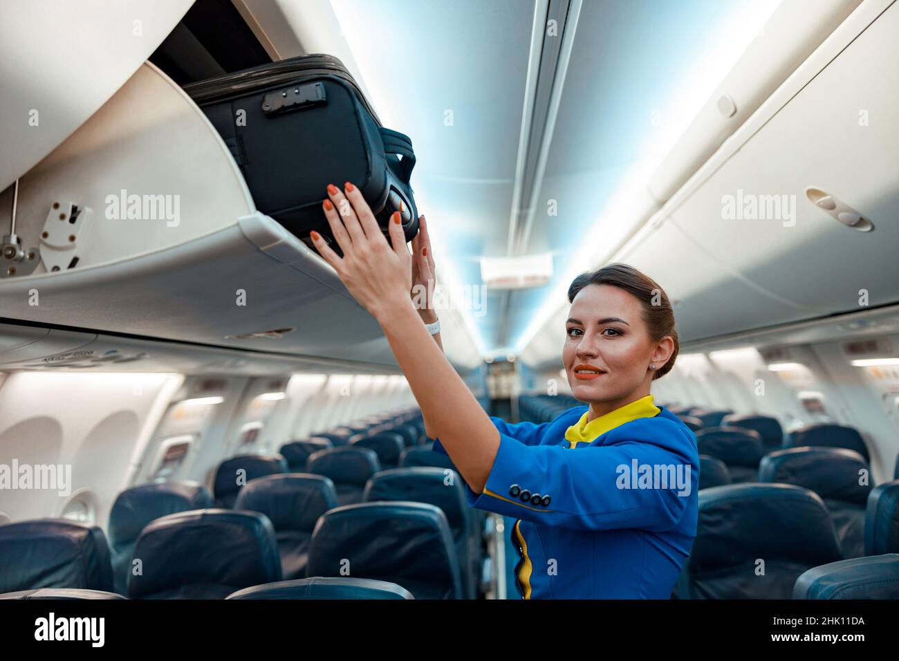 Stewardess putting travel bag in overhead luggage bin in aircraft Stock