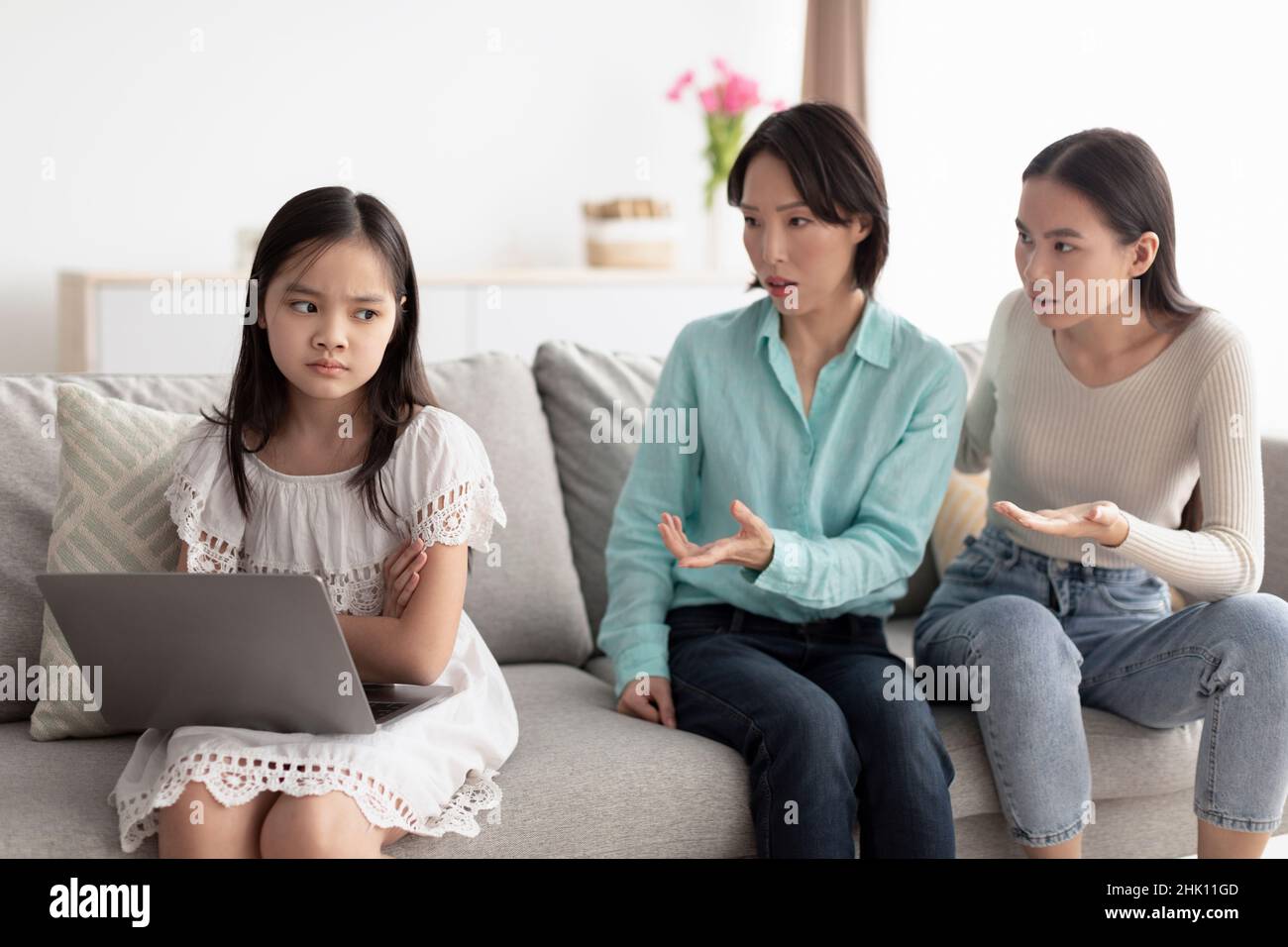 Gadget addiction in little kids. Asian girl with laptop being scolded by  mother and grandmother for pc overuse at home Stock Photo - Alamy