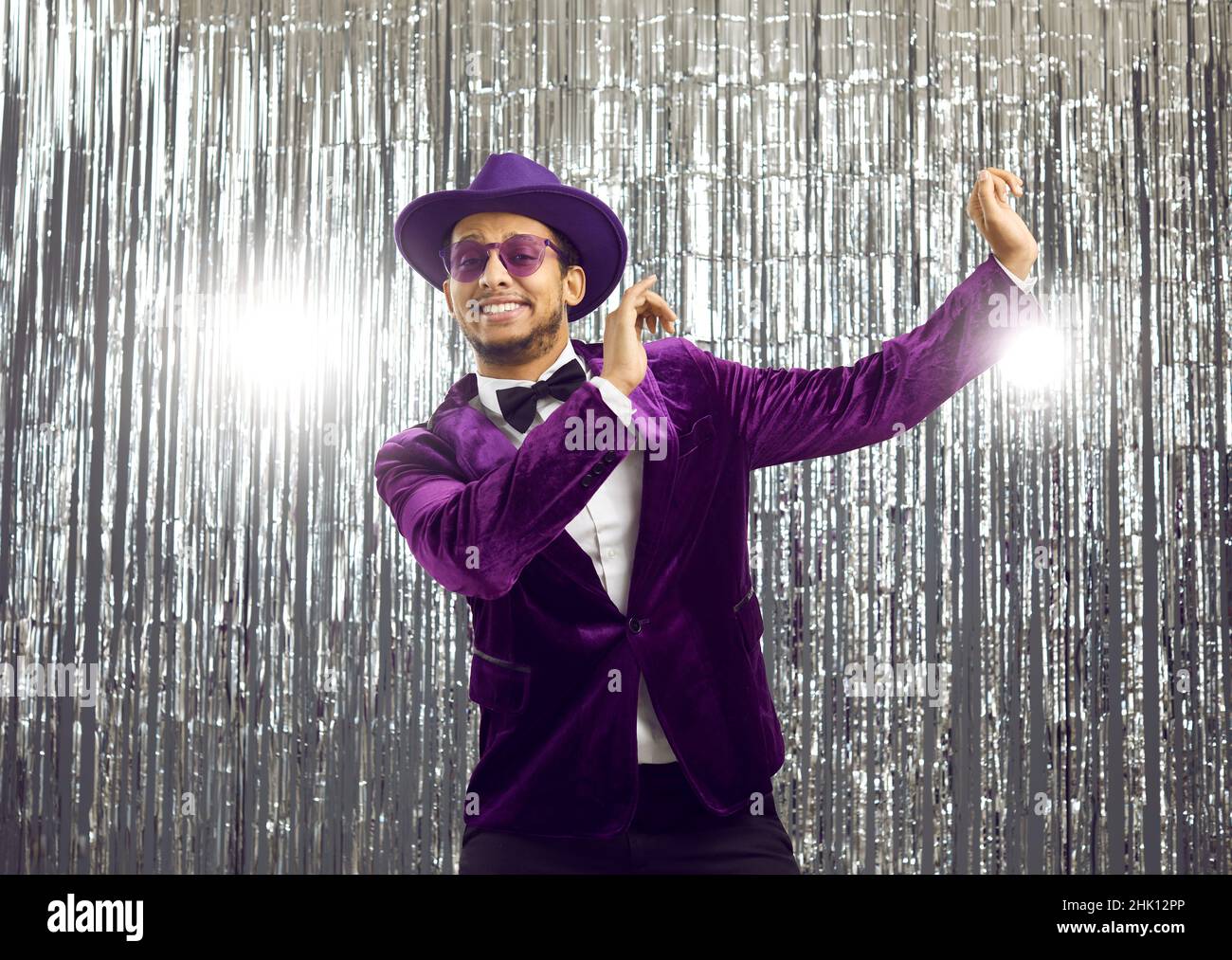 Happy goofy young man wearing a funny purple jacket and hat dancing at a disco party Stock Photo