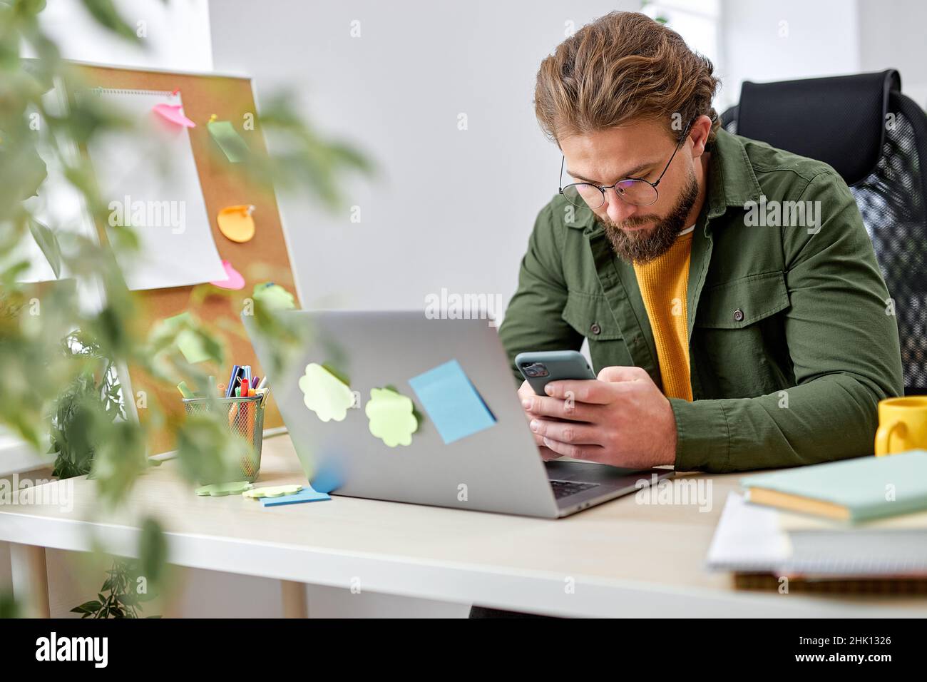 young businessman holding smartphone sitting in office. caucasian manager ceo using cell phone mobile apps and laptop. Digital technology applications Stock Photo