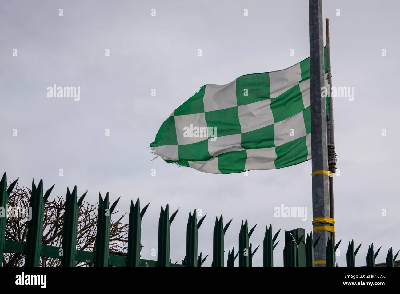 A white and green flag hung from a metal fence Stock Photo