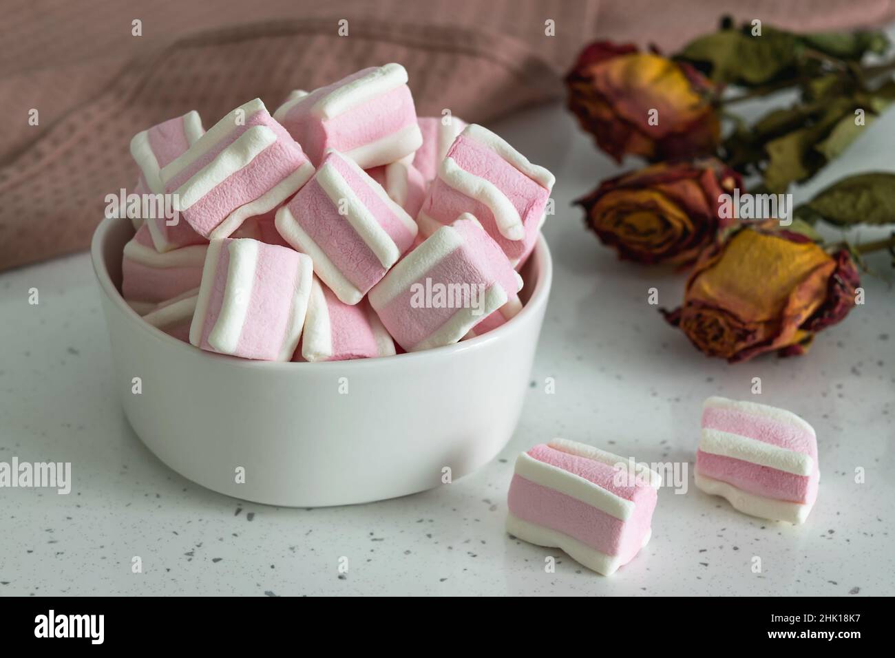 White-pink marshmallow on a light table next to a bouquet of wild field dried flowers. Sweets for tea and coffee on a porcelain plate. Horizontal phot Stock Photo