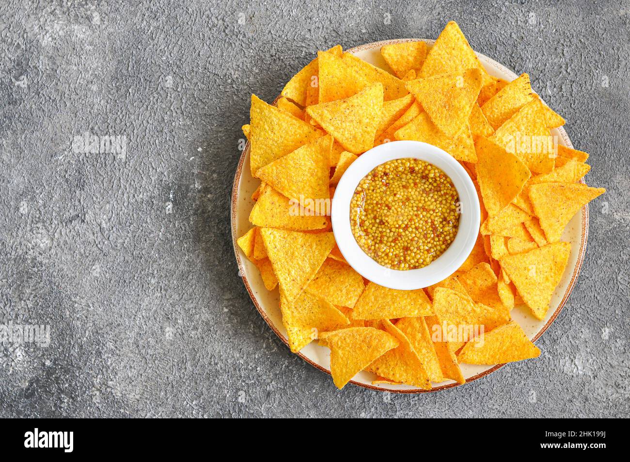 Corn tortilla chips with french mustard served in big plate on a gray background. Top ivew. Stock Photo