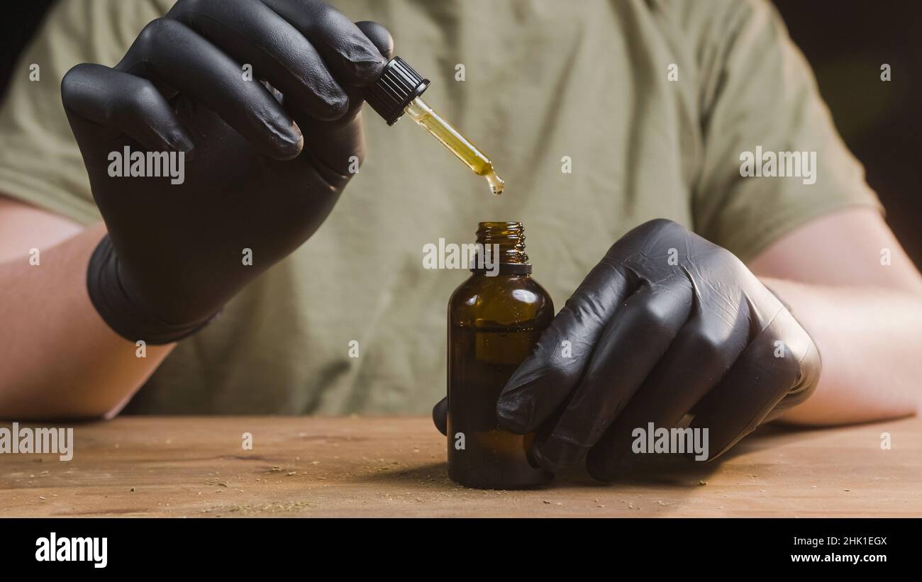 Hands dripping CBD oil drops in glass bottle with a pipette. Stock Photo