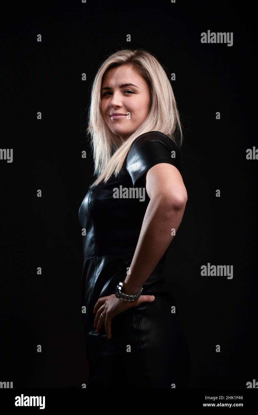 A beautiful blonde girl with long hair looks at the camera on a black