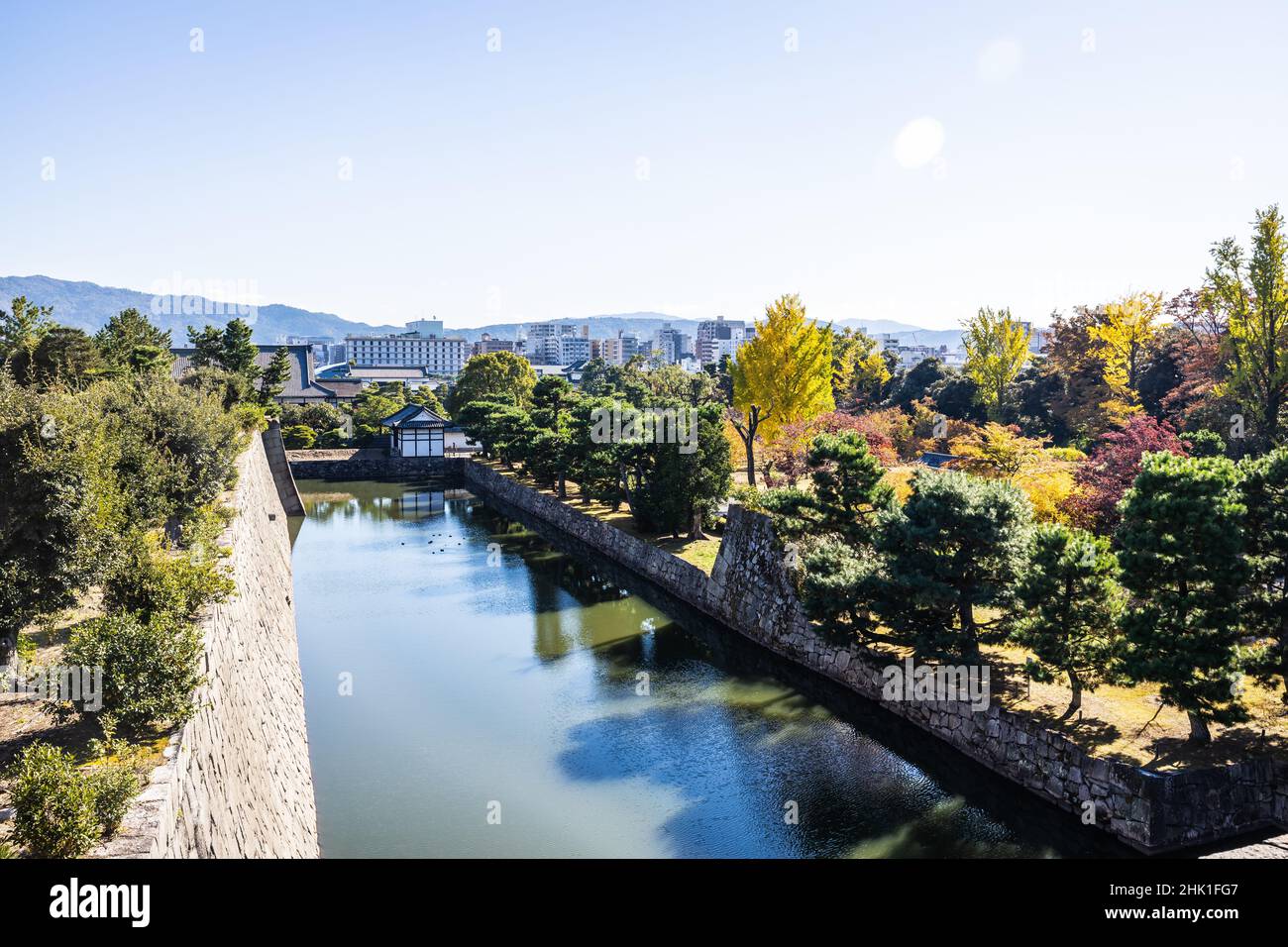 The moat of Nijo Castle with the city of Kyoto in the background and fall colors on the trees in daylight. Stock Photo