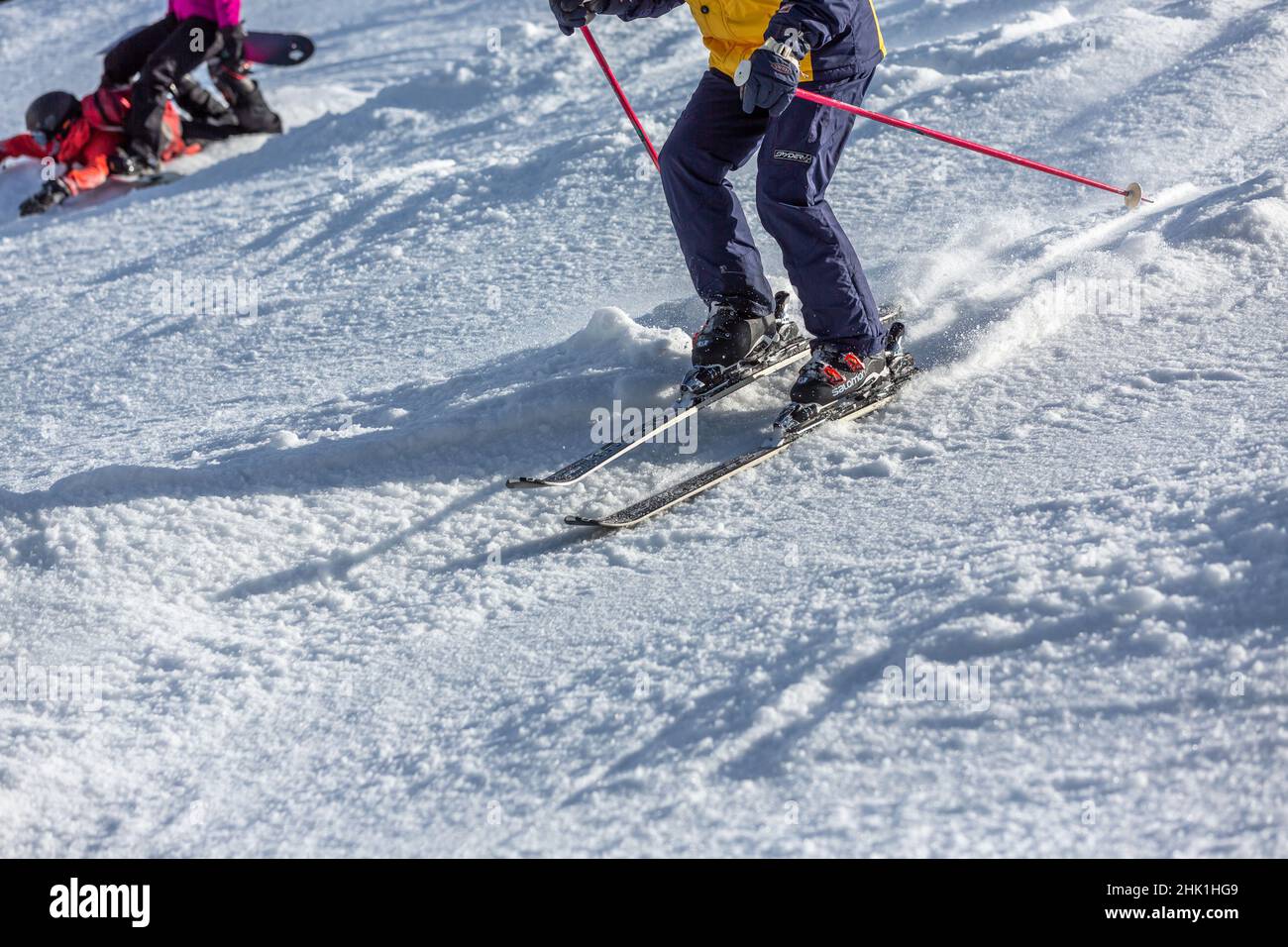 skiers next to fallen snowboarder on the slope Stock Photo