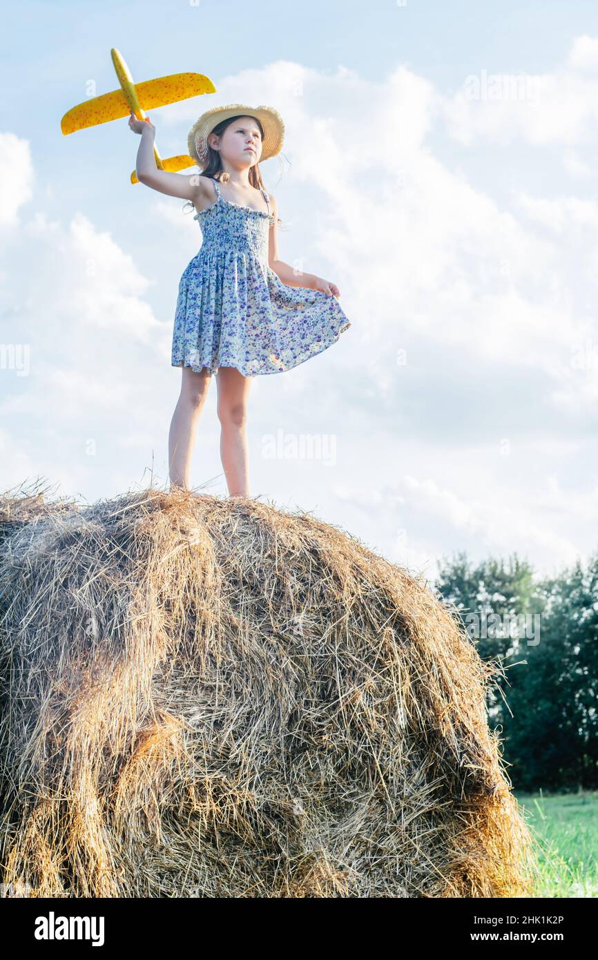 Portrait of little girl playing, standing on haystack in field. Flying ...