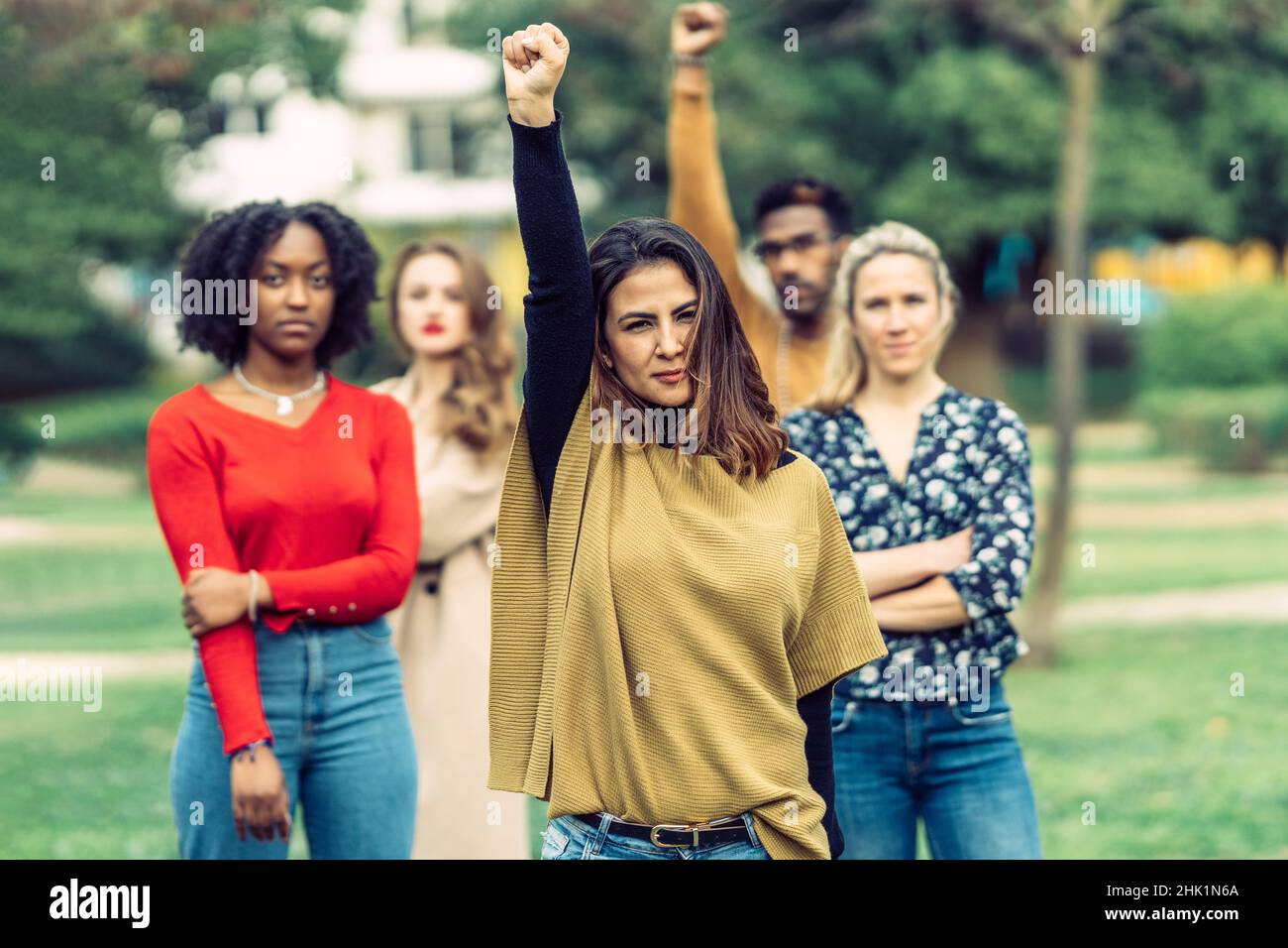 woman with latin features raises her fist protesting inequality between men and women with 4 people behind her  Stock Photo