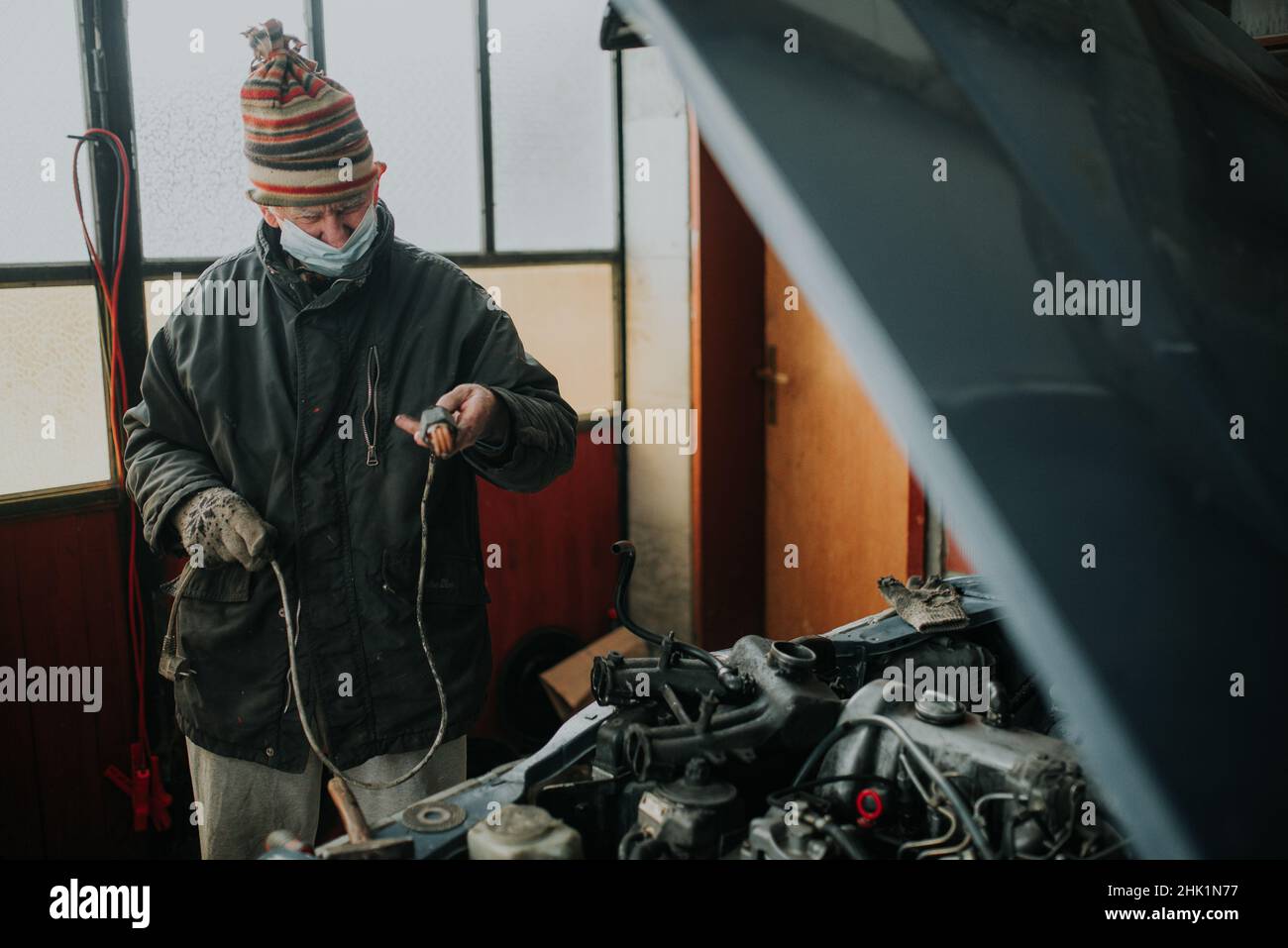 Old man with protective mask in the garage repair his old car. Stock Photo