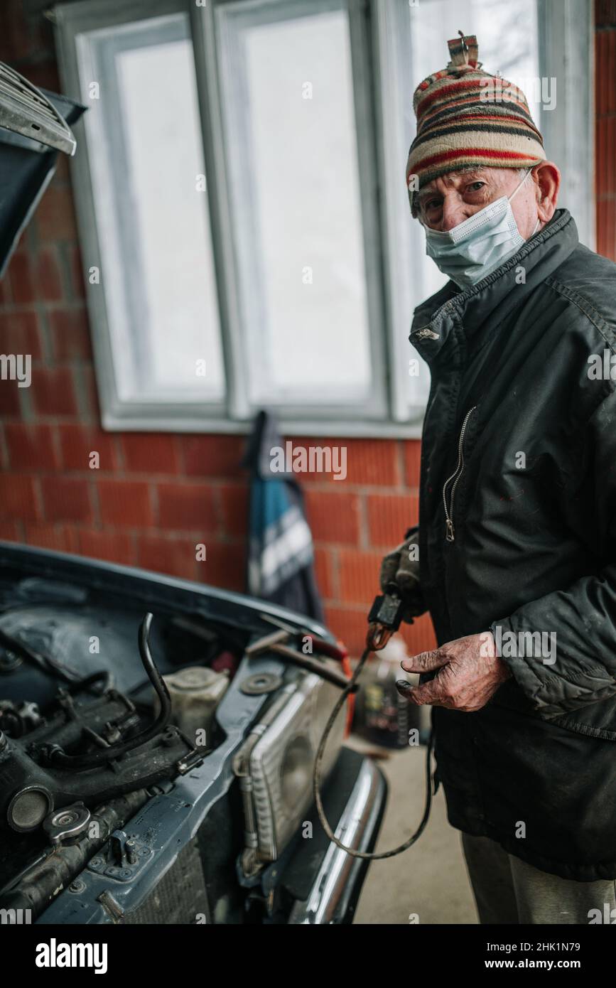 Old man with protective mask in the garage looking at camera. Stock Photo