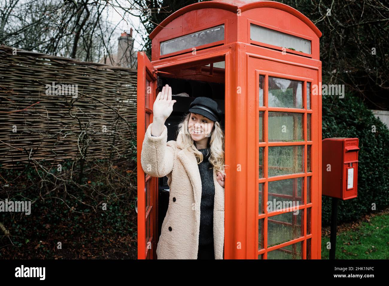 woman doing the queens wave out of an English telephone box Stock Photo