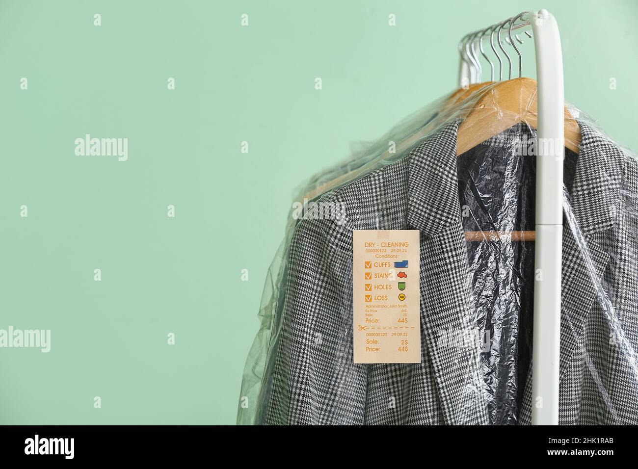 Rack with clean checkered jacket in plastic bag on green background ...