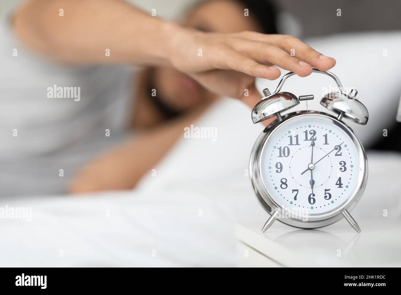 Time To Wake Up. Man Reaching Alarm Clock On Bedside Table, Closeup Stock Photo