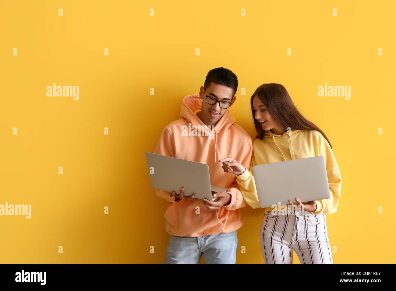 Young couple using laptops on yellow background Stock Photo