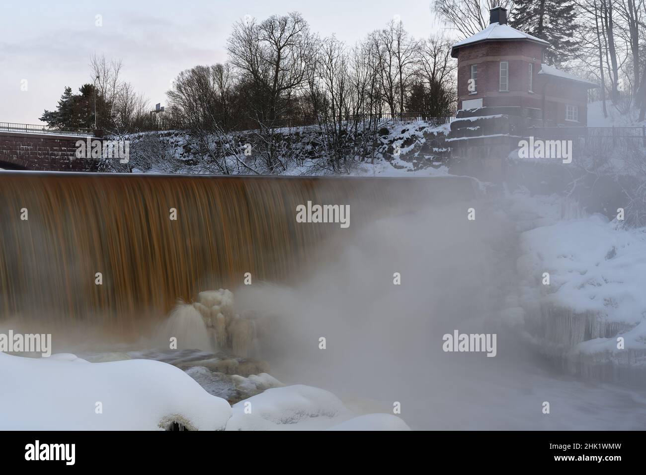Helsinki, Finland - March 10, 2021: Water pours over frozen museum dam in the mouth of Vantaa River at the Vanhankaupunginkoski rapids (Vanhankaupungi Stock Photo