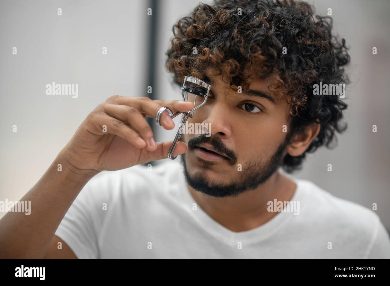 Serious concentrated young man using a lash-curler Stock Photo - Alamy
