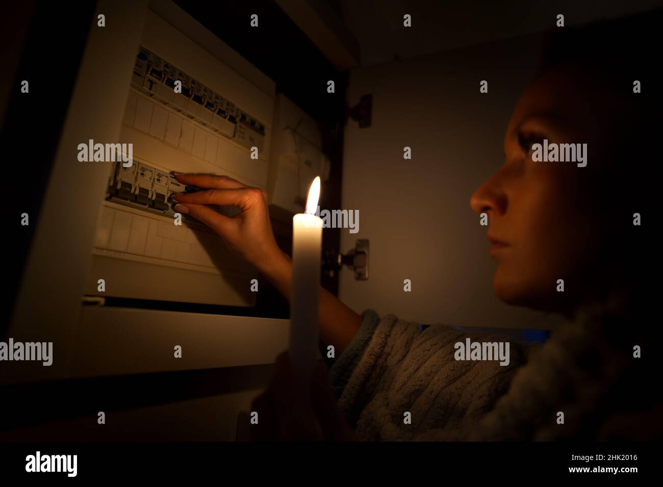 Woman in total darkness investigating fuse box at home during power outage or blackout. No electricity concept Stock Photo