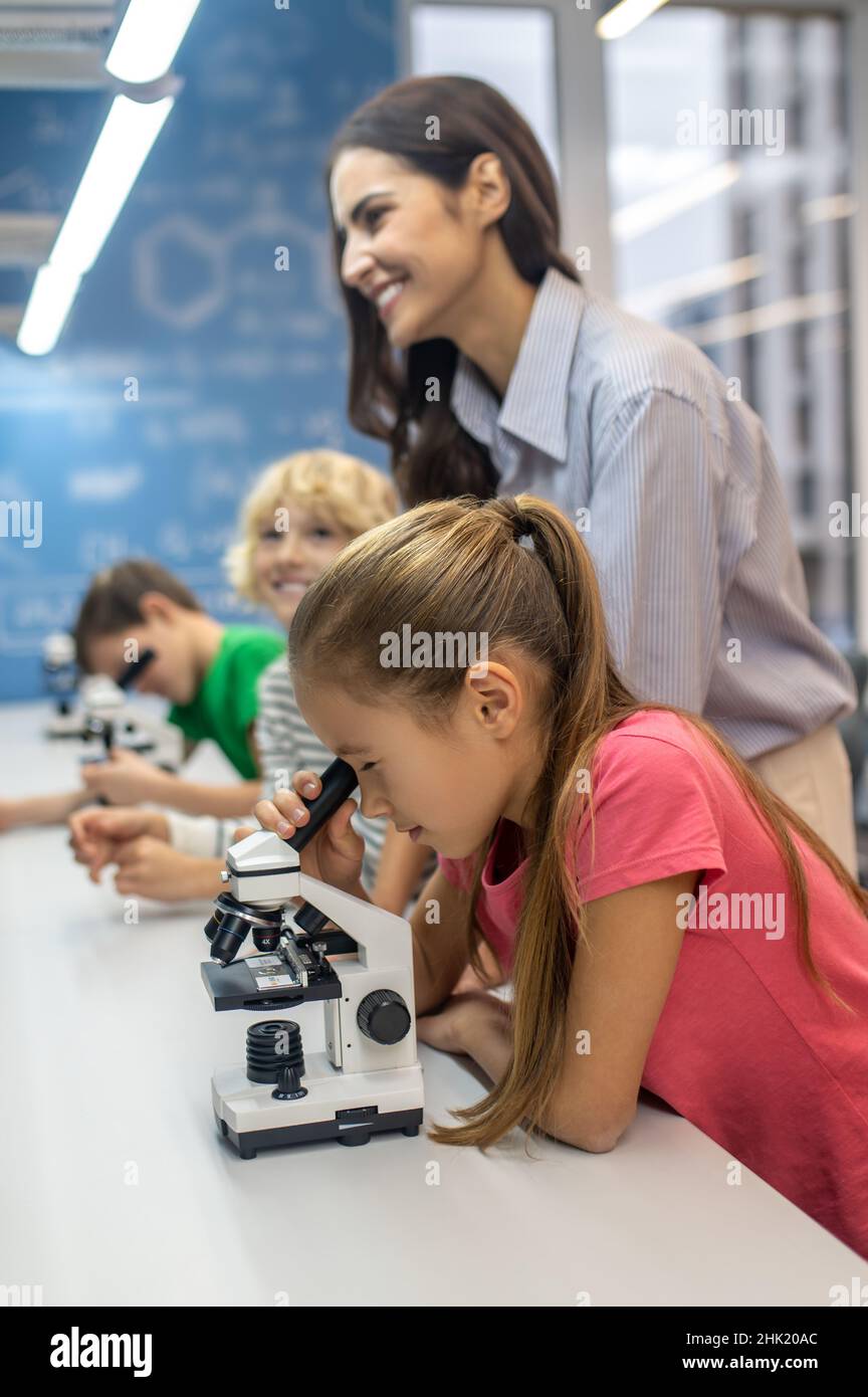 Girl looking through microscope and teacher with boys Stock Photo - Alamy