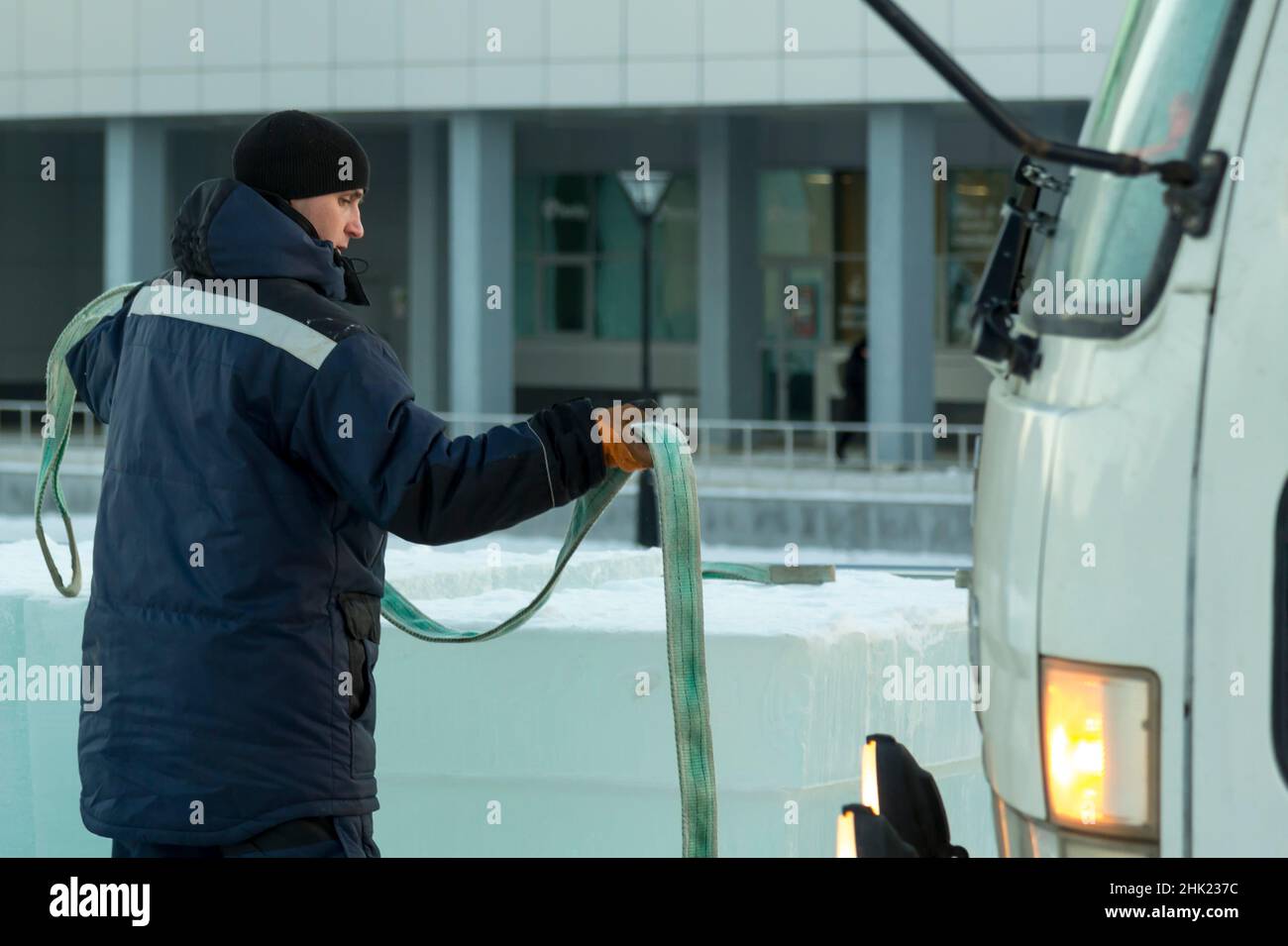 Portrait of a worker in a winter jacket and a black knitted hat with a tape sling in his hands Stock Photo