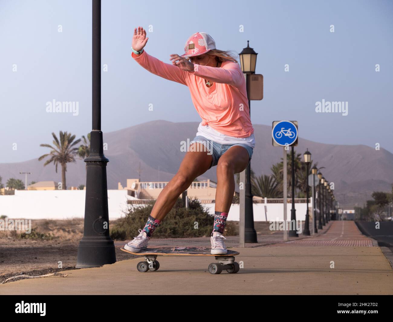 Caucasian skater woman sliding on skateboard. She is wearing a hut and short jeans Stock Photo