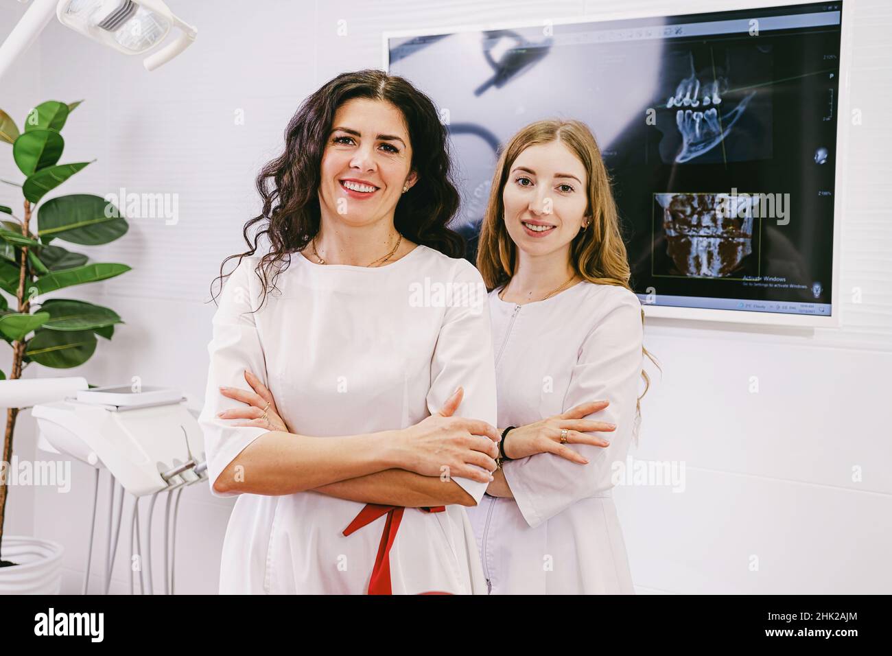 Two doctors dentists woman happy looking at the camera wearing white uniform standing in the office clinic with tooth snapshot at the computer over Stock Photo