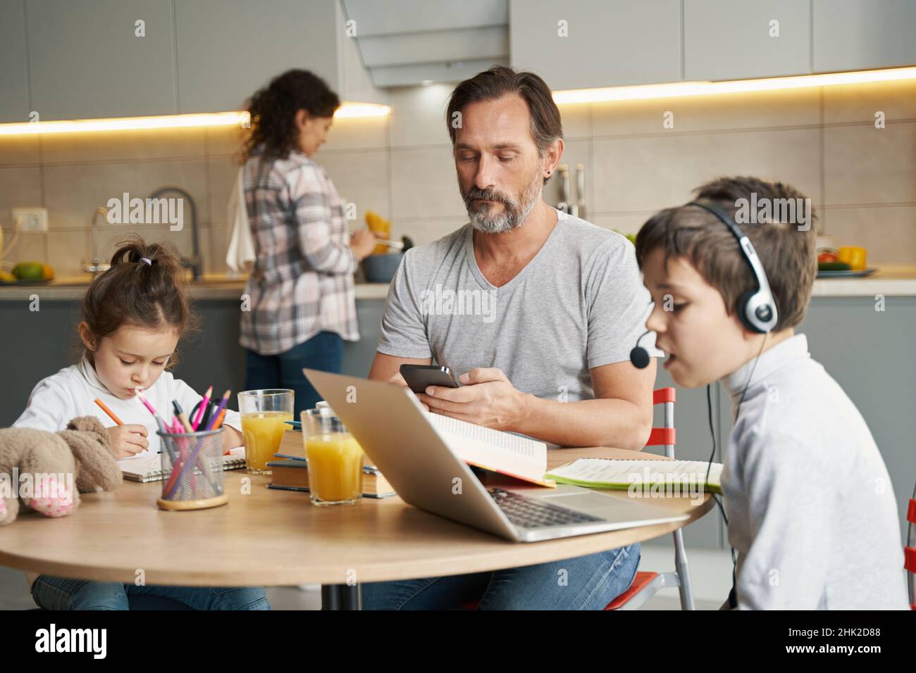 Father using smartphone while his kids doing homework Stock Photo