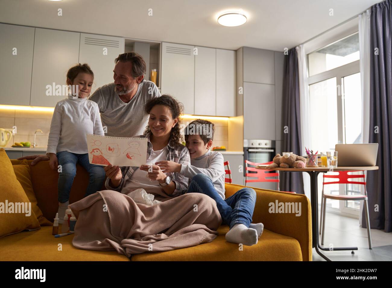 Mother sitting with son on sofa and enjoying daughter drawing Stock Photo