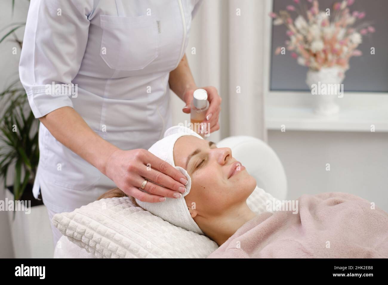 Cosmetologist cleaning skin with cotton pad, care and treatment procedure in modern aesthetic clinic. Woman applies tonic on face in beauty salon Stock Photo